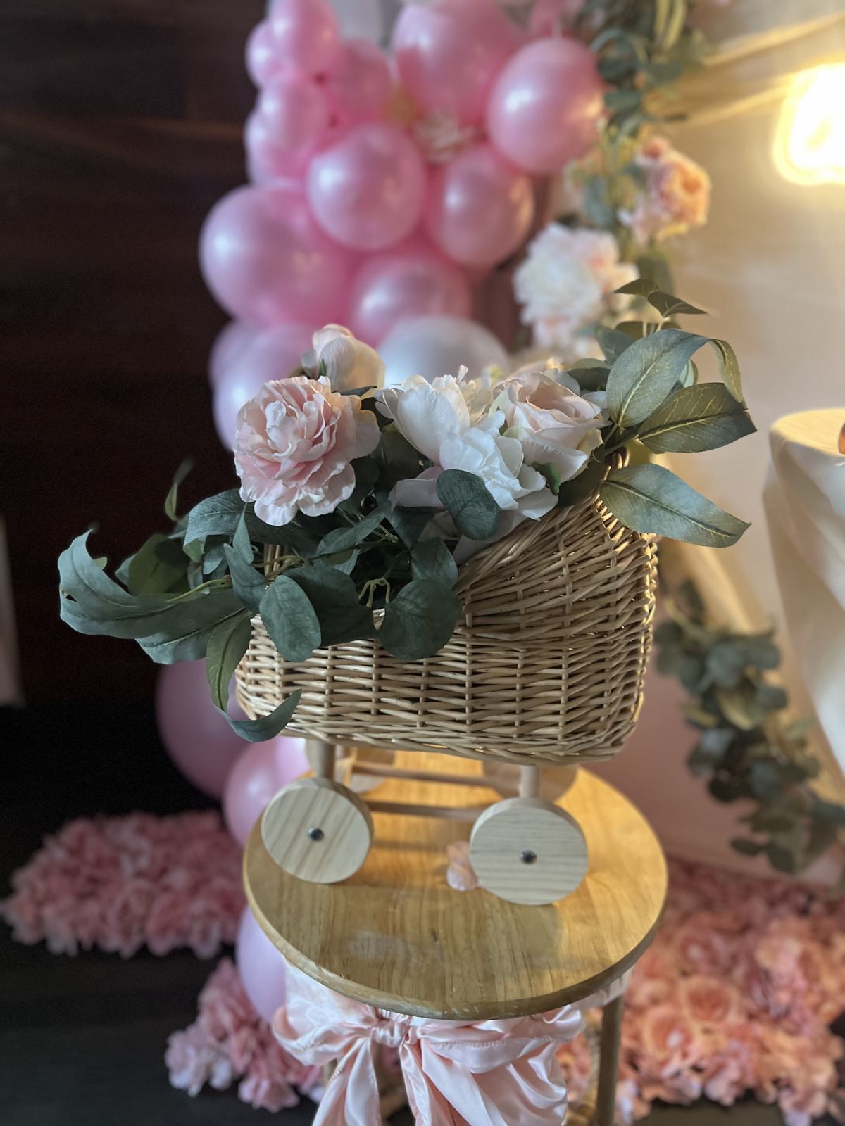 A wicker pram filled with roses and eucalyptus, set among pink balloons