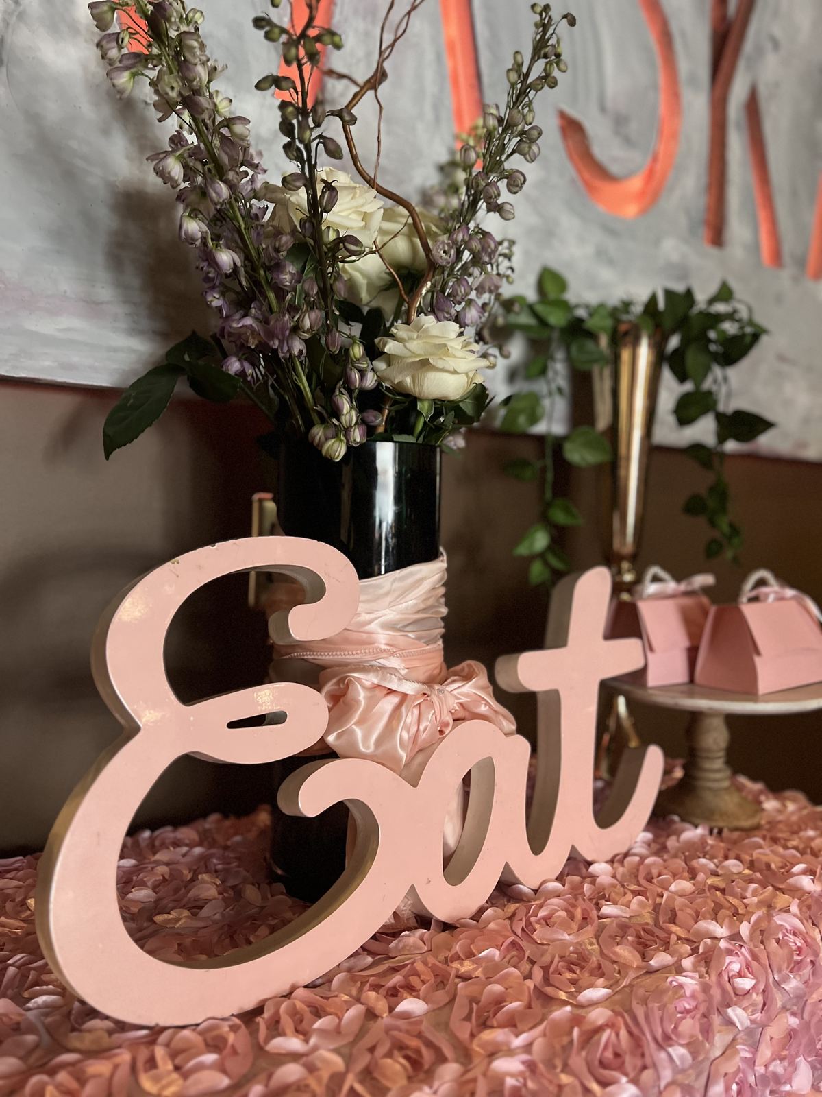 Flowers and an Eat sign on a table at Kaskade, with the restaurant's painted sign behind